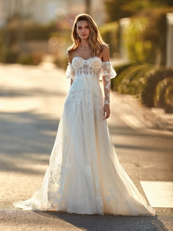 Romanticism embodied in a sensational glimmery tulle dress with lace and a strapless sweetheart neckline. An ultra-feminine design that enhances the sensuality of the neckline and shoulders with long removable sleeves that are slightly gathered on top. 