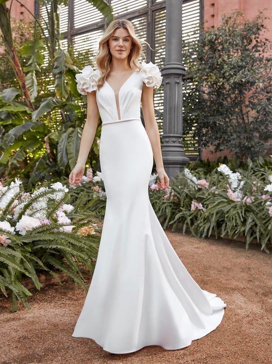 Folds of soft crepe create gorgeous sleeve accents in the form of rosettes, and add extra length to this svelte mermaid style dress that features a ruched bodice and chapel train.  