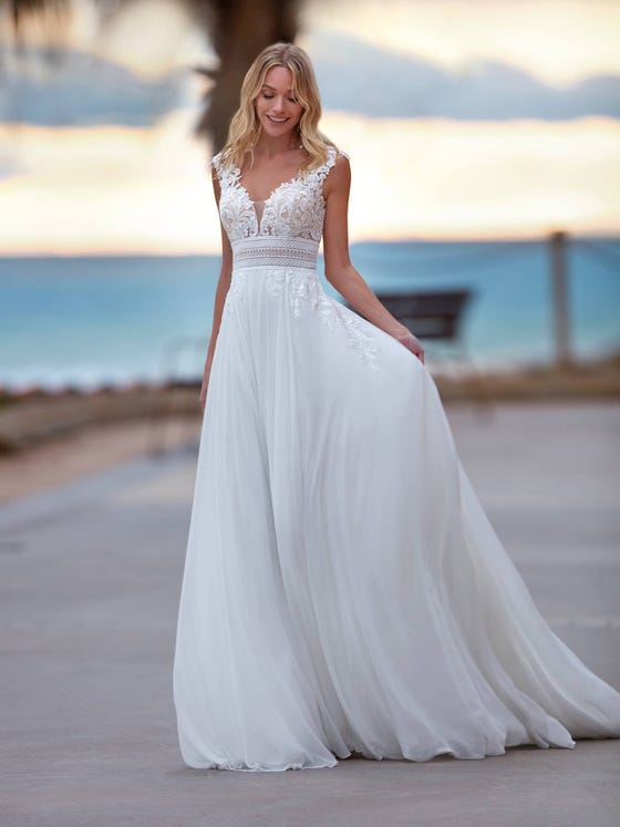 A bohemian style overtakes this incredible dress with a flowy chiffon skirt. A design with an original guipure and beading waistband with a V-neck front and back, where the transparencies and glimmers give it a very special feel. 