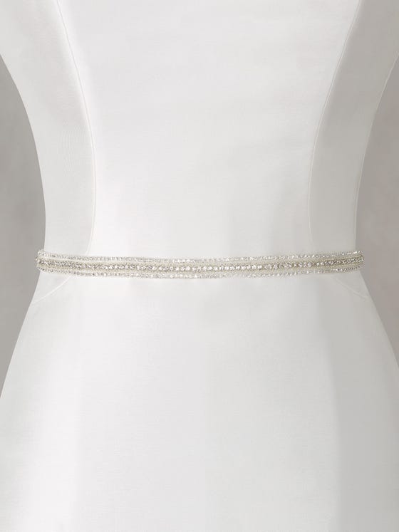 Cinturón de efecto bordado en gasa con pedrería brillante, creando unas cenefas que se sobreponen en la cintura como si formasen parte del vestido. 