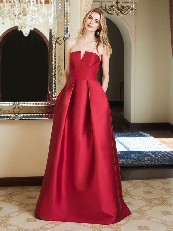 A modern ballroom gown in glossy Mikado. The wide pleats on the skirt create a formal silhouette, and the structured bodice has a scoop back and asymmetrical, crossover sash.  