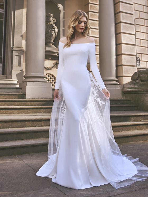 An unusual mermaid design. The play of the off-the-shoulder neckline combined with the illusion back and long sleeves gives the dress a mystical feel. A design you can wear with the tulle train and create a dégradé effect from the back. 