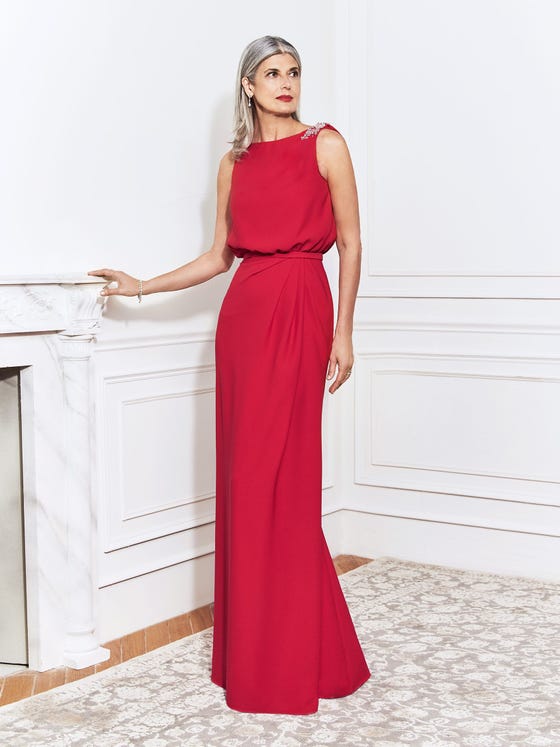 Sheath gown crafted in cherry red crepe, featuring relaxed, bishop bodice with bateau neckline and silver beading at the shoulders, all tied together with a fitted waistband on a streamlined skirt. 