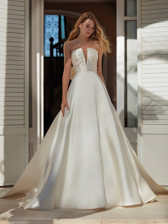 Elegance and sophistication merge in this princess-cut Mikado dress with a spectacular sleeveless neckline, plunging V-neck and sensational draped effect on the chest. To give it more volume, you can add a large bow on the skirt. 