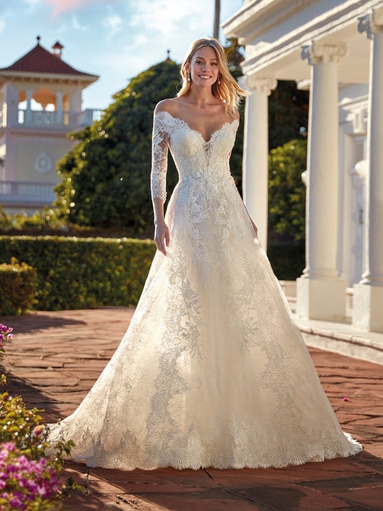 Sophisticated A-line lace dress with a flattering off-the-shoulders V-neck and three-quarter sleeves. A design that plays with the romanticism of the fabric and the sensuality of transparencies to dress a very special bride. 