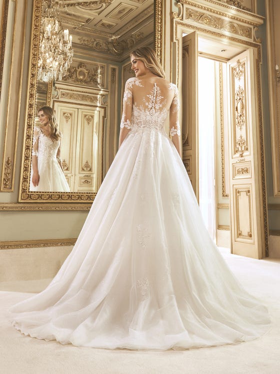 Tradition and sophistication. A princess dress with a tulle skirt and beaded floral appliques that blend with the semitransparent bodice, with three-quarter sleeves and an illusion back. 