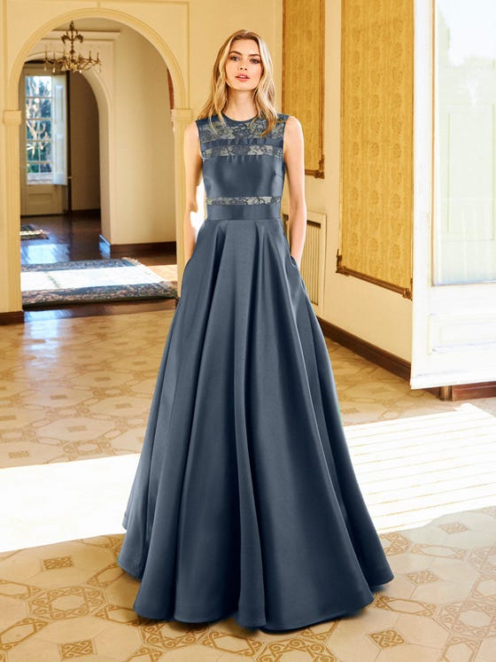 Elegantly formal, this princess style gown in glossy Mikado has a full, softly pleated skirt and demure boat neck bodice embellished with lace inserts. Deep pockets add an on-trend accent.  