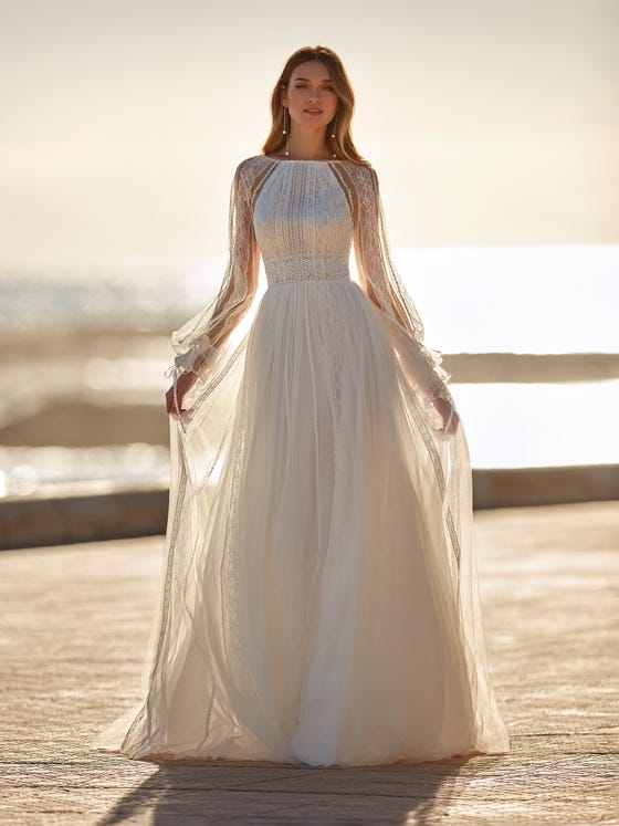 Romanticism becomes a dress with a tulle design and guipure appliques. A dress with a flowy skirt and square back that captures the limelight with a round neck with transparencies and long bishop sleeves that start from the neck. 