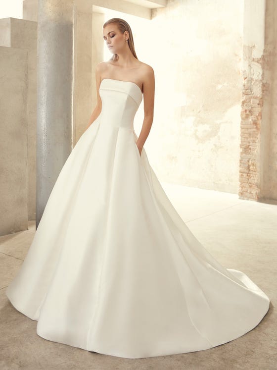 An iconic princess silhouette in glossy Mikado; formed by a strapless bodice and fashionable deep pockets.  With a classic chapel train and full skirt with flattering front darts.  