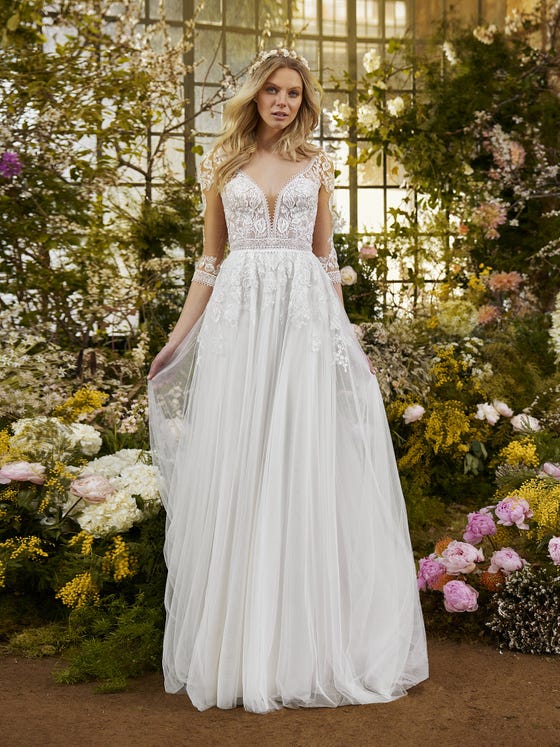 A wonderful illusion back matching the three-quarter sleeves finished with guipure. Floral details decorated with beading and guipure details wrap around the waist. A beautiful dress with a tulle skirt and flowers that cascade down, creating a waterfall effect. 