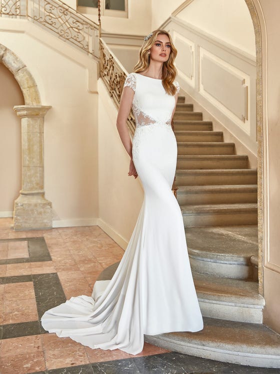 Meticulously placed lace inserts update an iconic mermaid gown in soft crepe. With a seductive illusion back, demure cap sleeves and chapel train in flowing georgette.  