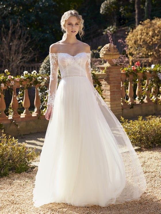 The draped effect of the bodice enhances your femininity, accentuating the delicacy of the sweetheart neckline. The long under-the-shoulder sleeves also highlight that sensuality and contrast with the lightness of the tulle skirt. 