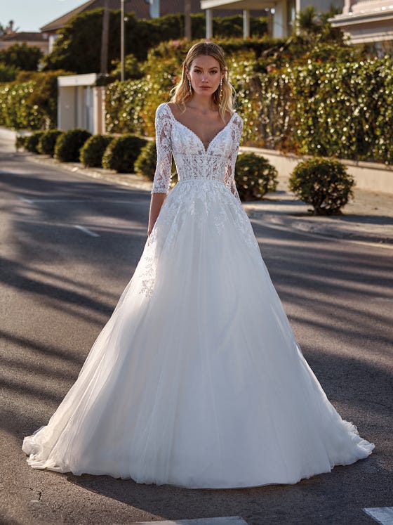 Elegance and romanticism. A beautiful princess-cut tulle dress with lace appliques creating a dégradé look on the skirt to match the decorations on the bodice with a V-neck front and back and three-quarter sleeves. 