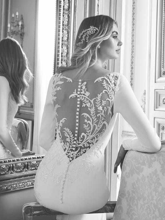 The elegance of crepe merges with floral embroidery and an illusion back to create this sensational mermaid silhouette with long sleeves. A dress that manages to combine minimalism and seduction. 