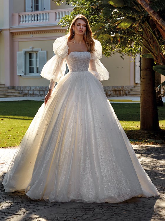 Feel like a fairytale princess in this beautiful glimmery tulle dress with pearls. A dazzling, spectacular dress with a draped, fitted bodice and a sleeveless neckline. You can accessorize the look with the oversize puffy sleeves matching the glittery fabric and beading. 