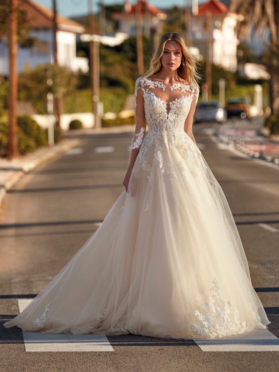 Beautiful princess-cut tulle dress with lace and beading appliques enveloping the bateau-neck bodice, with an original play of crystal tulle transparencies and floral details decorating the neckline, back and three-quarter sleeves. 