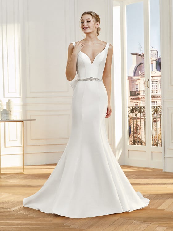Gorgeous wedding gown in matte Mikado, crafted with a sloped, V neckline, flattering cuts, and a dramatic trumpet silhouette that nicely complements the voluminous, statement bow at the back. 