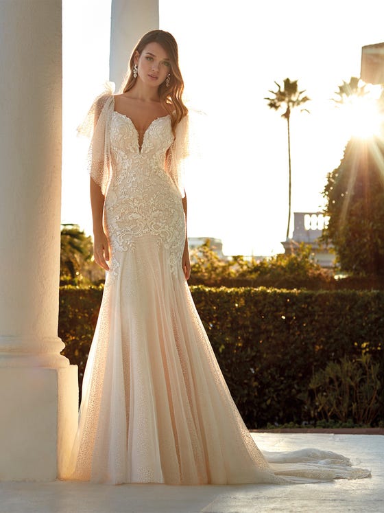 Spectacular and highly romantic tulle mermaid dress with glimmers of glitter and gold thread decorating the entire dress, creating a highly feminine and seductive silhouette. The V-neck combines with the removable ruffle-style sleeves which cascade down the arm. 