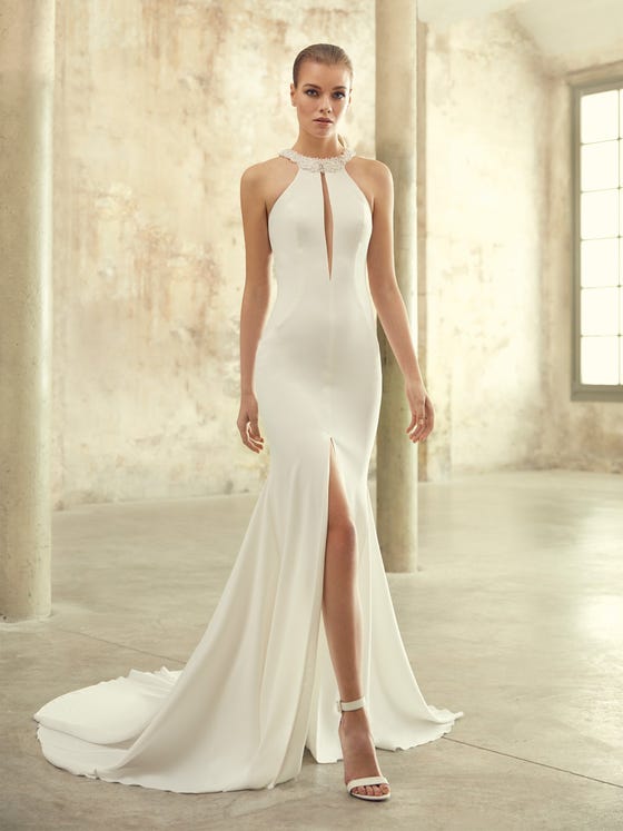 A sophisticated halter neck gown with a classic mermaid cut and sensual front split. Crystal beading adorns the neck, while row buttons and geometric straps frame your shoulder blades beautifully.  