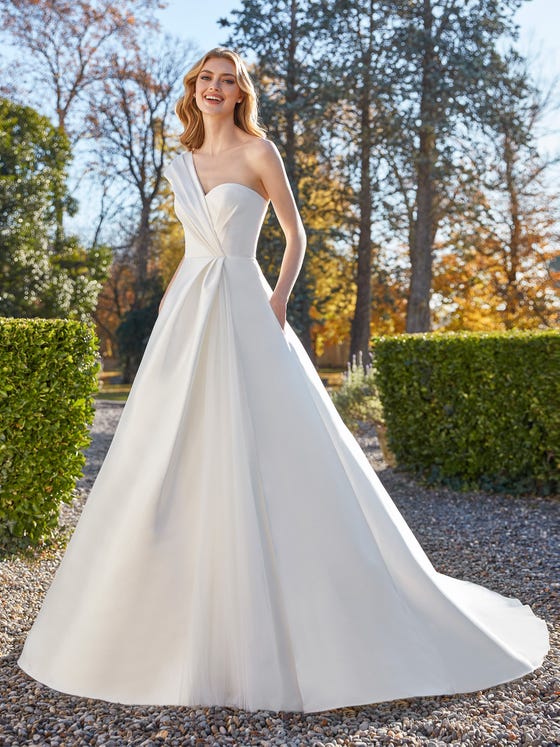 A classic princess cut with a voluminous skirt gets an update with an asymmetrical shoulder accent and gentle puckering around the waist area. With deep pockets and a seductive sweetheart neckline.  
