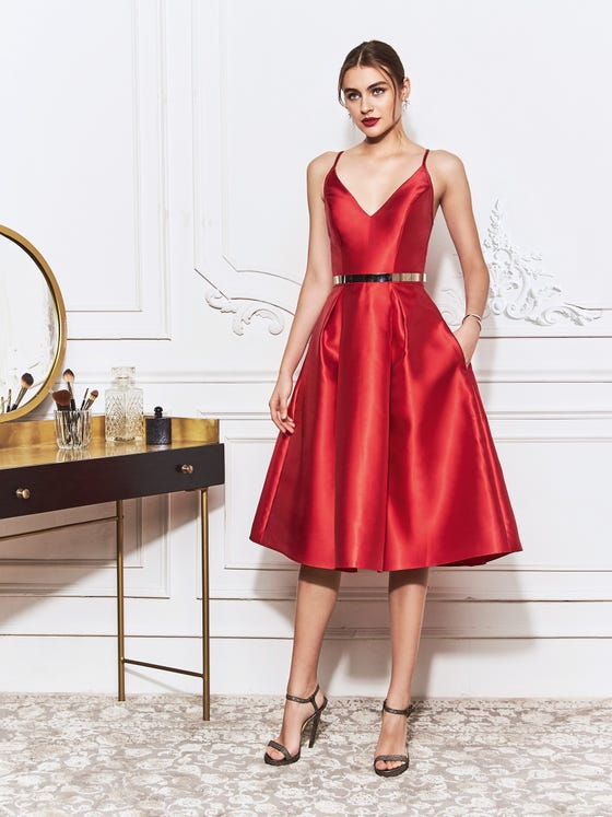 This short princess gown comes in a glossy, cherry red, crafted from classic Mikado with a V-neck bodice and spaghetti straps that cross at a feminine open back, culminating in a gorgeous billowing skirt. 