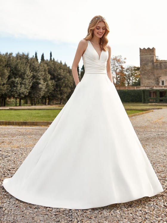 A fun and fresh take on a classic A-cut gown with flattering folding around the lower bodice and a nude illusion back scattered with pearls. With fashionable pockets and a floor-sweeping chapel train 