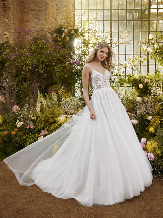 Delicate and dainty. A design that enhances the femininity of your silhouette, contrasting the princess skirt in glimmery tulle with an incredible fitted bodice that plays with transparencies and lace details and crossed beaded straps. Floral motifs and sparkles cascade down from the neckline to the train. 