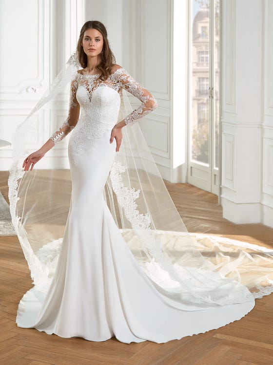 Elegant cuts of netted, French lace blossom about the three-quarter tattoo sleeves, off-the-shoulder illusion neckline, and white crepe bodice of this mermaid dress, which finishes in a delicate line of buttons down the back. 