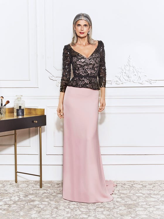 This sheath gown glitters with a sophisticated, black bodice of sequined  embroidery, featuring a sleek waistband and peplum accent over a base of soft, powder pink crepe with an elegant train. 
